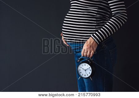 Pregnant female with vintage alarm clock expecting baby in third trimester of pregnancy