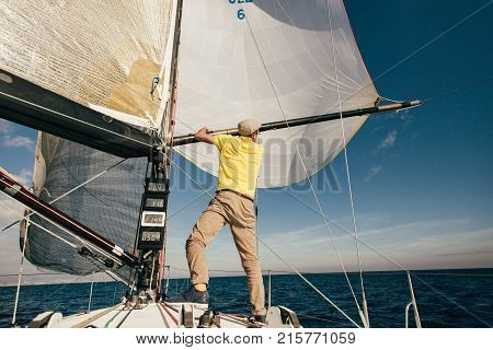 Professional sailor or yachtsman uses mast and forestay to put up spinnaker or mainsail on racing competition yacht or sailboat on warm summer day
