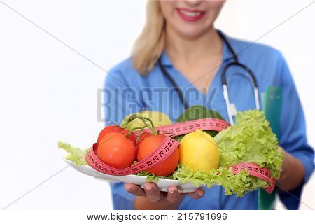 Portrait of a female doctor of a nutritionist with vegetables and fruits on a plate in hands. Isolated on white background