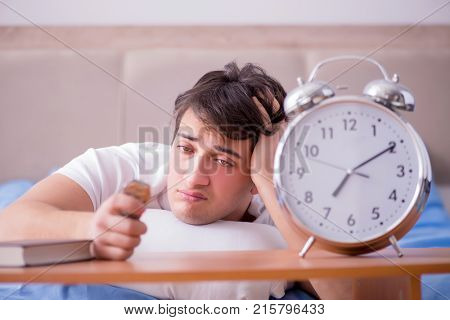 Man in bed frustrated suffering from insomnia with an alarm cloc