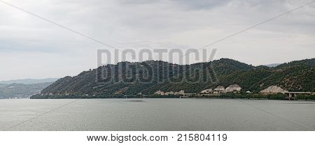 A picturesque landscape with a river bank covered with forest and road along the shore. Panoramic view of the point where the Cerna River meets the Danube southwestern Romania's Mehedinti County.