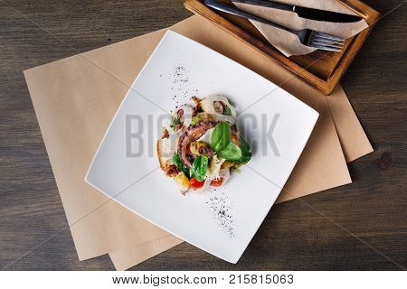 Salad with octopus and vegetables top view. Appetizing fresh mediterranean seafood meal with toasts, restaurant serving
