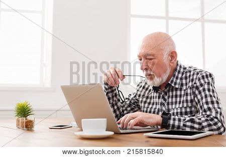 Mature man using laptop and writing in notepad at home desk. Education, recipe concept