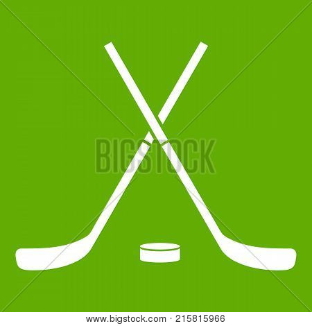 Crossed hockey sticks and puck icon white isolated on green background. Vector illustration