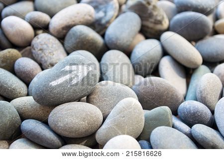 Abstract smooth round pebbles sea texture background with a white arrow pointer on the stone