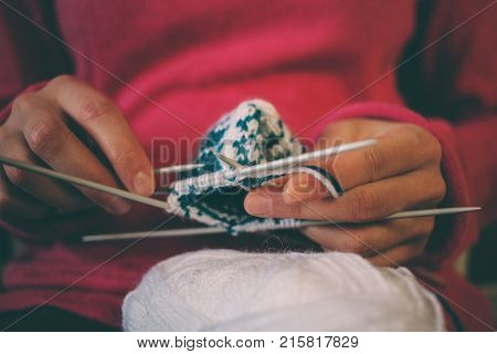 The woman knits knitting. Female hands hold the skein of thread and knitting needles. Fingers knitters. Mittens with jacquard pattern.
