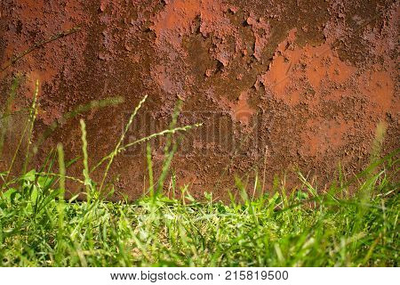 Rusty brown old metal background and a lower border of green grass. Corrosion texture. Focus on the rusty wall