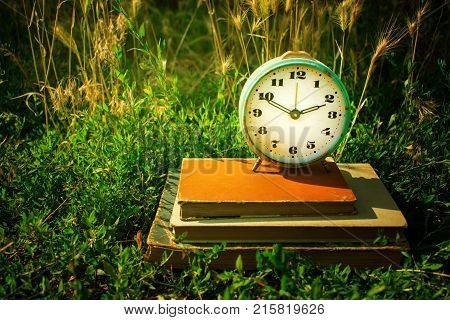 Vintage alarm clock on a stack of old books against a background of green grass. Copy space. Time concept business planning.
