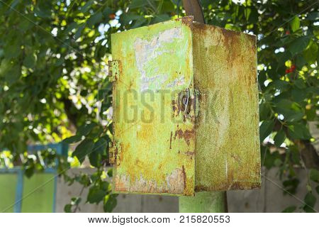 Old rusty green peeling metal postal box (junction box) under the lock on the background of green leaves