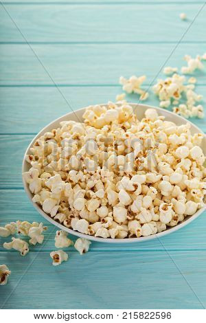 Cheddar cheese salted popcorn in a white bowl on light blue table