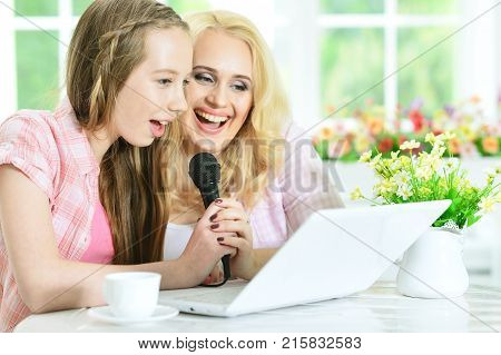 mother and daughter sitting at table and singing karaoke with laptop