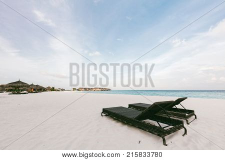 Two lawn chairs standing on a sandy beach on a seashore. Outdoor relaxation. Maledives travel
