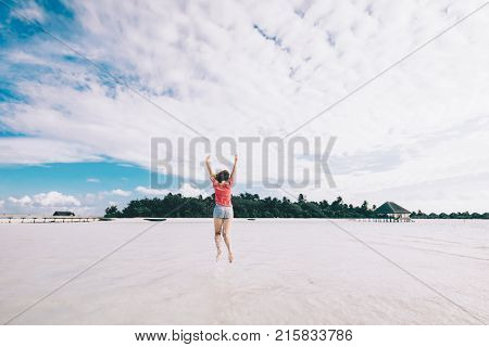 Girl jumping on a sandy beach. Tropical island. Excitement and joy gesture. Maledives fun moments