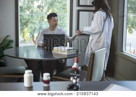 Female scientist in a lab coat researching with her male coed med school student in a campus laboratory. The woman is learning science and technology in medical industry.