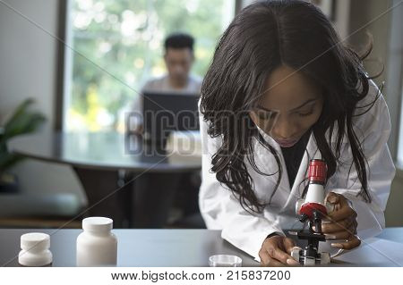 Female scientist in a lab coat researching with her male coed med school student in a campus laboratory. The woman is learning science and technology in medical industry.