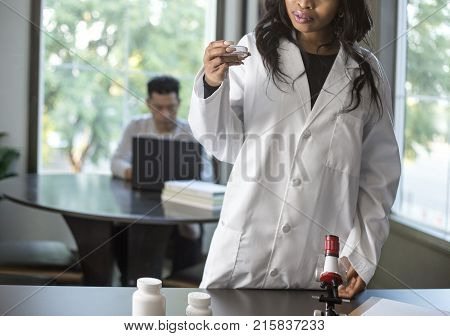 Female scientist in a lab coat researching with her male coed med school student in a campus laboratory. The woman is learning science and technology in medical industry.
