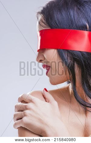 Caucasian Brunette Woman Posing with Red Ribbon Blinder on Eyes with Passionate Sensual Expression.Touching Lips with Tongue. Vertical Image