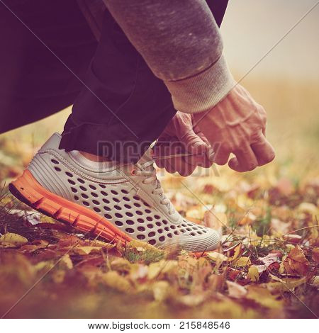 Closeup of man tying shoelaces on autumn grass in park. image with vintage toning
