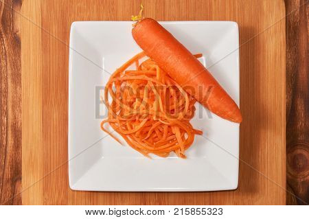 Grated and whole carrots in a white cup on a wooden background.