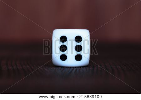 Single white plastic dice on brown wooden board background. Six side cube with black dots. Number six.