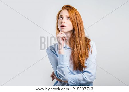 Let me think. Pensive uncertain young Caucasian female keeping hand on her chin and looking up sideways with indecisive unsure expression, feeling hesitant about what to wear for a walk or date