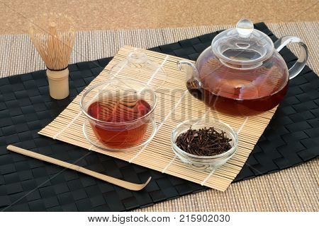 Healthy Japanese kuchika roasted twig tea with glass teapot and cups, stirrer and whisk on bamboo background. Has many health benefits including rejuvenating properties.