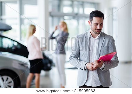 Handsome young salesman at car dealership selling vehichles