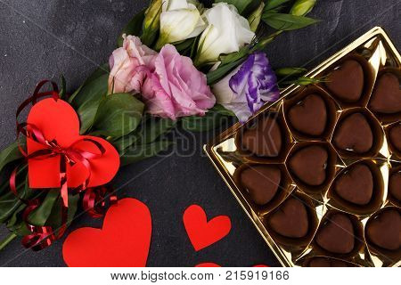 A bouquet of Japanese roses and a box of chocolates is not completely shown with carved hearts on a stone background. The view from above is close up