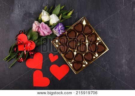 A bouquet of Japanese roses tied with a ribbon and a box of chocolates and carved hearts on a stone background. View from above