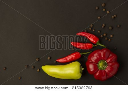 A few ripe red peppers sweet and hot and spices pepper peas on a black background
