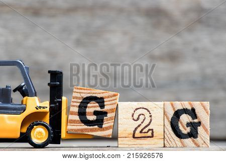 Yellow plastic forklift hold letter G to complete word G2G (Government to government) on wood background
