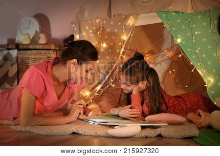 Young mother with little daughter reading book in hovel at home