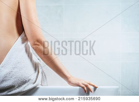 Woman sits on the edge of bathtub close up image