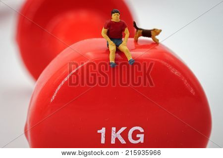 Sport and fitness concept. Man runner miniature figure running on red 1kg dumbbell