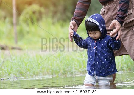 Cute girl child learning to walk on water river have adult help and holding her hands.