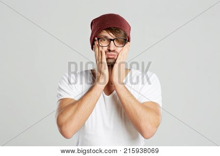 Waist up studio portrait of a bearded man posing with his hands to his face looking upset copyspace unhappy emotions pity pitiful unhappy sad disappointed expressive concept.