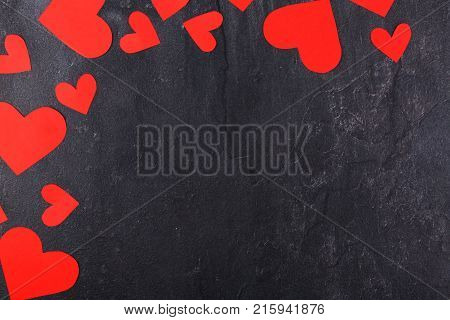 The hearts are red, cut out in different sizes, in a semicircle in the upper left corner on a stone background