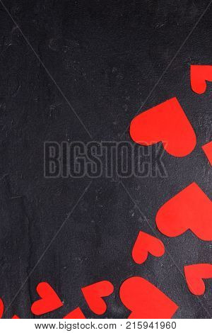Red hearts cut out in different sizes lie in a semicircle in the lower right corner on a stone background
