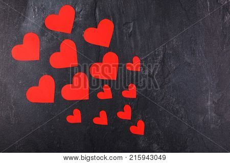 Red hearts of different sizes go from the smaller to the larger diagonally to the left on a stone background