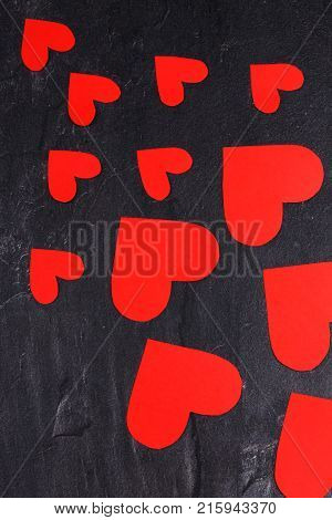 Red hearts of different sizes go from a smaller to a larger diagonal to the right down close-up on a stone background