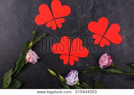 The hearts are red, carved in different sizes lined up in butterflies close-up and bottom of Japanese roses on a stone background. View from above