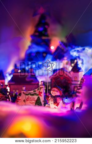 Seasons greeting sign with smiling snowman holding star of bethlehem stands in front of a christmas village. Fairytale festive miniature scenery