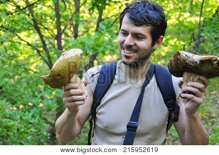 Portrait of man holding two giant porcini mushrooms. Happy man picking big boletus edulis or cap mushrooms in forest