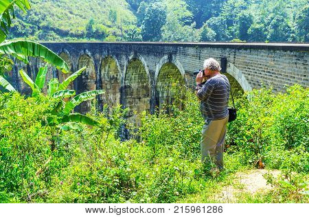 The tourist makes the pictures of the Nine Arch Bridge from the edge of the Damodara Ella Sri Lanka.