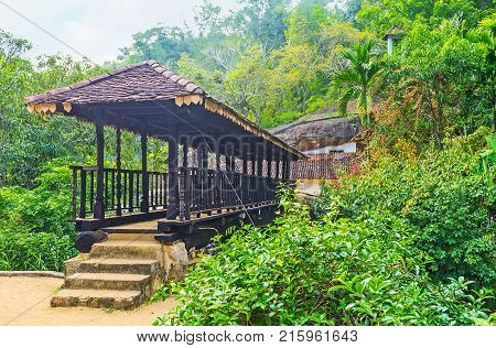 The carved ancient Bogoda Wooden Bridge with tiled roof is surrounded by lush greenery Ketawala Sri Lanka.