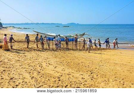 BENTOTA SRI LANKA - DECEMBER 6 2016: The fishermen's crew pull the net standing in line on the sand coast on December 6 in Bentota.