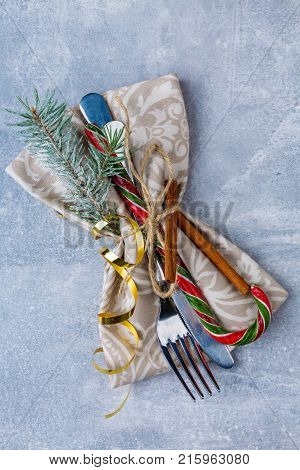 Cutlery knife and fork wrapped in a cloth serving napkin and decorated with Christmas candy, golden ribbon, fragrant cinnamon sticks and small branches of the Christmas tree. View from above.