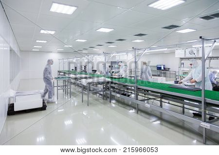 factory workers in white lab suits and face masks, producing tv sets on assebly line with some modern equipment