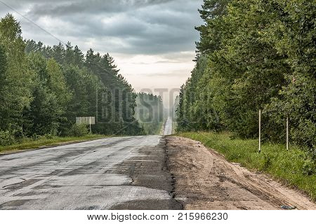 Kaluga oblast Russia Road is not far away from Yukhnov. Morning the old surface road forest clouds fog.