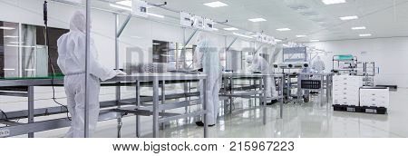 factory workers in white lab suits and face masks, producing tv sets on assebly line with some modern equipment